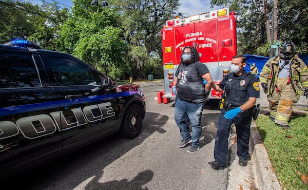 Protester Jordan Mazurek, 28, who cemented his hands in two 55-gallon plastic drums filled with concrete outside of the Governor's Mansion, is escorted by a Tallahassee Police Department officer in handcuffs to a vehicle, Friday, April 17, 2020. Mazurek is protesting how Gov. Ron DeSantis is handling coronavirus in state prisons. (Alicia Devine/Tallahassee Democrat via AP)