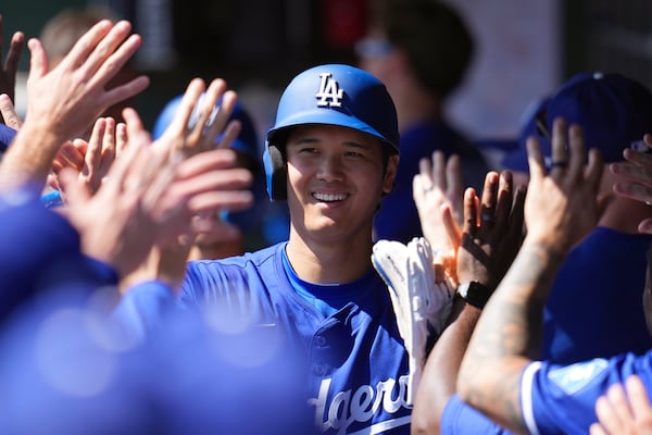 Los Angeles Dodgers' Shohei Ohtani, of Japan, smiles as he celebrates with teammates after scoring a run on a two-run home run by Dodgers' Tommy Edman during the first inning of a spring training baseball game against the Cleveland Guardians, Tuesday, March 11, 2025, in Phoenix. (AP Photo/Ross D. Franklin)