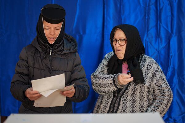 An elderly woman with poor eye sight holds a stamp after getting help from her daughter, an Orthodox nun, left, to cast her vote in the country's presidential elections, in Pasarea, Romania, Sunday, Nov. 24, 2024. (AP Photo/Vadim Ghirda)