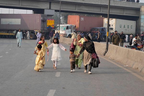 Travellers walk to cross an area barricaded by authorities ahead of a planned rally by supporters of imprisoned former premier Imran Khan's Pakistan Tehreek-e-Insaf party, in Lahore, Pakistan, Sunday, Nov. 24, 2024. (AP Photo/K.M. Chaudary)