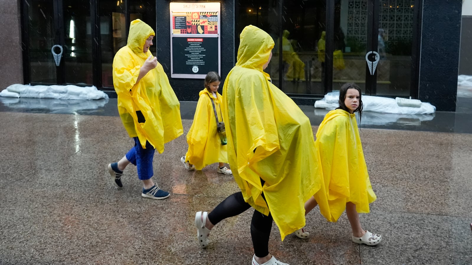 Tourists walk past a sandbagged store entrance as they exit the Disney Springs entertainment complex before the arrival of Hurricane Milton Wednesday, Oct. 9, 2024, in Lake Buena Vista, Fla. (AP Photo/John Raoux)