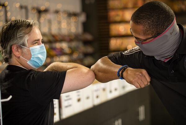 COVID precautions include the newly-invented elbow bump replacing the handshake. The bump is practiced by Infinite Realities owner Chris Brennaman, left, and loyal customer Detective Robert Byars. PHOTO: Jenni Girtman for The Atlanta Journal-Constitution