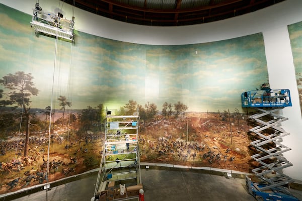 Conservators on scissor lifts complete the restoration of “The Battle of Atlanta,” including adding back one of the vertical sections that was missing, seen at right. Artisans used chopsticks wrapped with cotton bolls to clean the mammoth painting. CONTRIBUTED: ATLANTA HISTORY CENTER