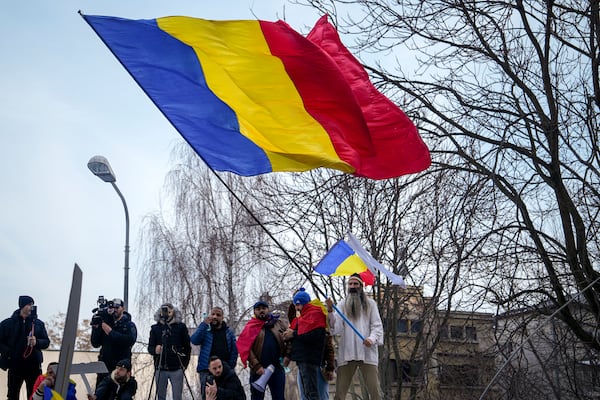 Supporters of Calin Georgescu, the winner of Romania's first round of presidential election, annulled by the Constitutional Court, wave the Romanian flag after Calin Georgescu was stopped in traffic and taken in for questioning, outside the General Prosecutor's Office, in Bucharest, Romania, Wednesday, Feb. 26, 2025. (AP Photo/Vadim Ghirda)