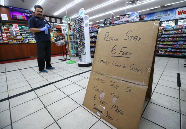 Ejaz Tarar stands next to his makeshift sign keeping customers 6 feet apart while cleaning the inside of the Food Mart in Newton County on  March 26, 2020, in Newborn. The store layed down tape to mark 6-foot barriers for customers. (Curtis Compton/ccompton@ajc.com)