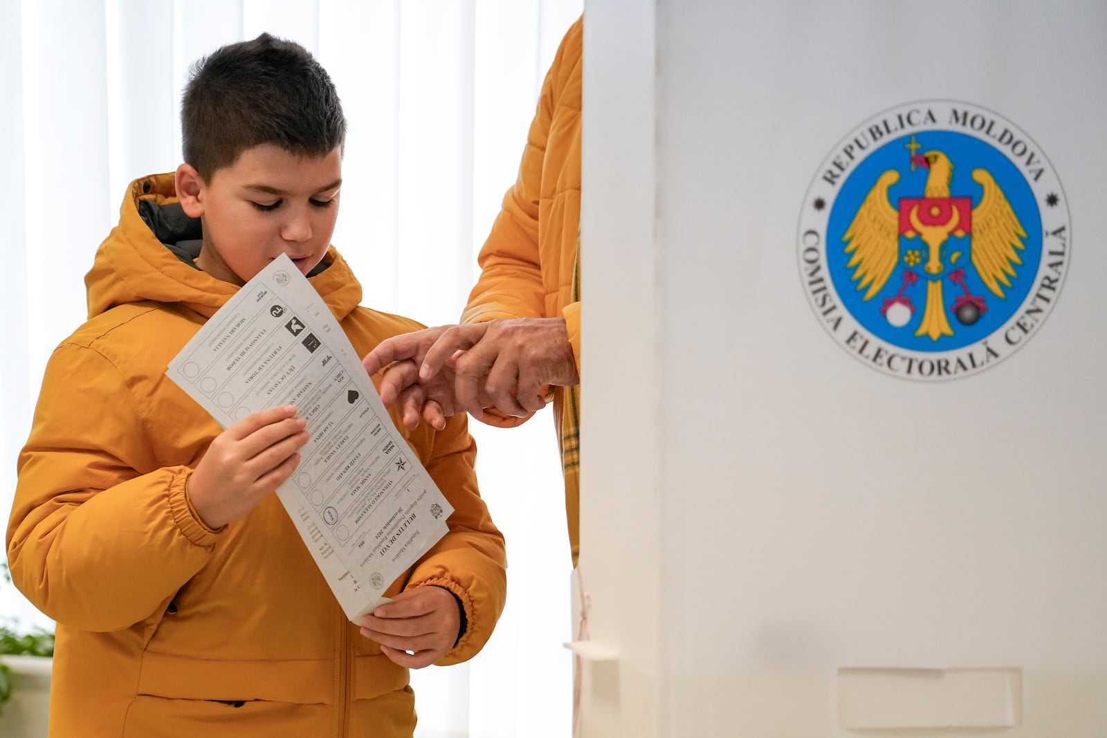 A child holds a voting ballot in Chisinau, Moldova, Sunday, Oct. 20, 2024, during a presidential election and a referendum on whether to enshrine in the Constitution the country's path to European Union membership. (AP Photo/Vadim Ghirda)