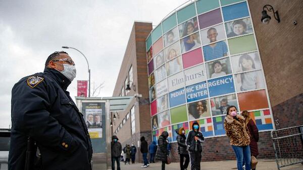 An NYPD officer wears personal protective equipment while maintaining order along a line to enter COVID-19 testing site at Elmhurst Hospital Center, Wednesday, March 25, 2020, in New York. (AP Photo/John Minchillo)