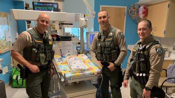 Three deputies visit the baby whose life they saved when she choked on fluids at a mall photo studio.