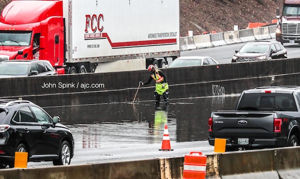 A worker clears a storm drain on I-285 in Dunwoody on Friday morning after heavy downpours caused water to pool on the interstate.