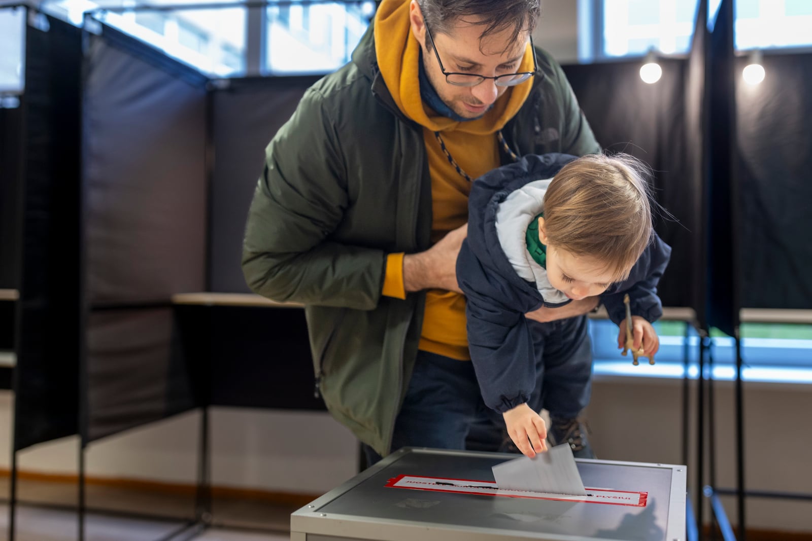 A man with a child casts a ballot at a polling station during a second round of voting in parliamentary election, in Vilnius, Lithuania, Sunday, Oct. 27, 2024. (AP Photo/Mindaugas Kulbis)