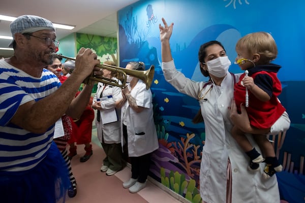 One-year-old Matheus Moreira is held by a health care worker as he watches clowns from the "Roda de Palhacos" cultural project perform during a carnival party at the pediatric area of the Servidores do Estado Federal Hospital in Rio de Janeiro, Tuesday, March 11, 2025. (AP Photo/Bruna Prado)