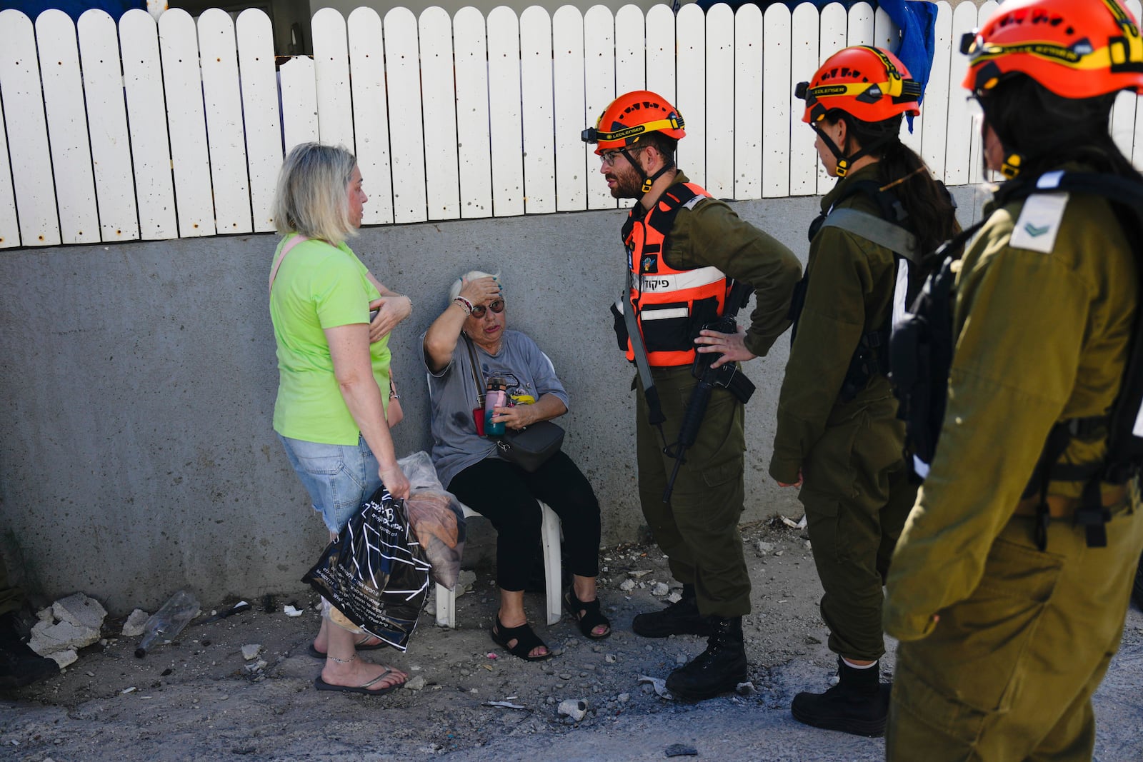 Israeli soldiers from the Homefront Command unit treat an elderly woman at the site that was hit by a rocket fired from Lebanon, in Kiryat Yam, northern Israel, on Tuesday, Oct. 8, 2024. (AP Photo/Ariel Schalit)