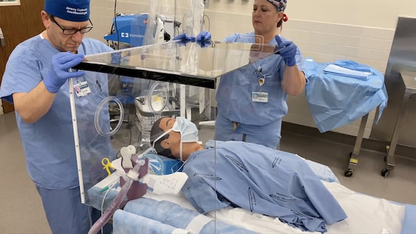 Dr. Cinnamon Sullivan, an assistant professor of anesthesiology at Emory University School of Medicine, and her colleague Dr. Jeremy Collins, an associate professor of anesthesiology, demonstrate how the four-sided box can be used to perform procedures such as intubating a patient who needs to be placed on a ventilator, and create a protective barrier for health care workers. CONTRIBUTED BY EMORY