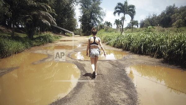 In this April 18, 2018 photo provided by Jan Snarksi, Snarski's wife Emilie Johnson carries their baby while walking toward Anahola Beach in Anahola on the island of Kauai in Hawaii. Kauai residents and businesses are still cleaning up from devastating floods and record rains, but community leaders are urging tourists to visit so residents don't suffer an economic calamity on top of the natural one. (Jan Snarski/@janmatthewsnarski via AP)