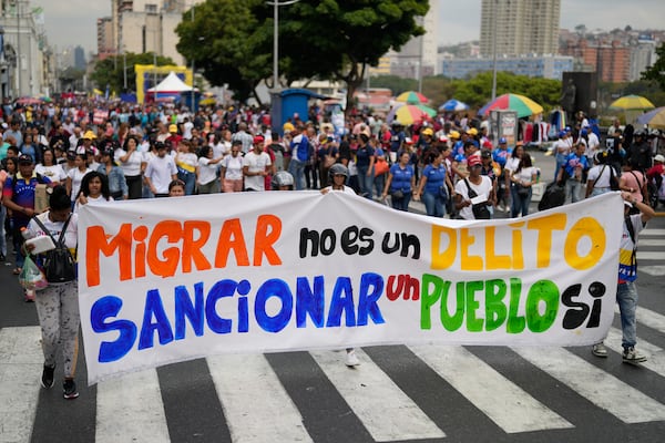 People hold a banner that reads in Spanish, "Migrating is not a crime; sanctioning a people is," at a government-organized march to protest the deportation from the U.S. of alleged members of the Venezuelan Tren de Aragua gang, who were transferred to an El Salvador prison, in Caracas, Venezuela, Tuesday, March 18, 2025. (AP Photo/Ariana Cubillos)