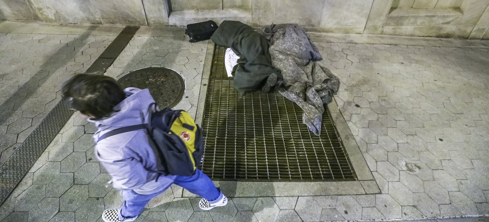 A Georgia State University student passes by two homeless men huddled on a grate blowing warm air on Auburn Avenue in downtown Atlanta. JOHN SPINK/JSPINK@AJC.COM