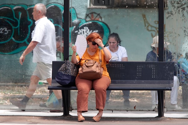 FILE - A woman tries to cool herself while waiting for a bus on a hot day in Skopje, North Macedonia, June 20, 2024. (AP Photo/Boris Grdanoski, File)