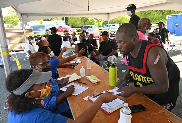 Kerwjuan Bailey (right) receives a $100 prepaid debit card from the DeKalb County BOard of Health's Audrey Moyer (left) after he got the COVID-19 vaccine shot during a vaccination event at The Gallery at South DeKalb in Decatur on Saturday, August 13, 2021. (Hyosub Shin / Hyosub.Shin@ajc.com)