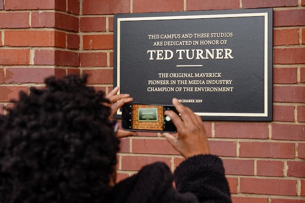 A woman takes a photo of a plaque on  an AT&T WarnerMedia building dedicating  it to Ted Turner, the founder of Turner Broadcasting System, on Friday, December 6, 2019, in Atlanta. (Elijah Nouvelage/Special to the Atlanta Journal-Constitution)