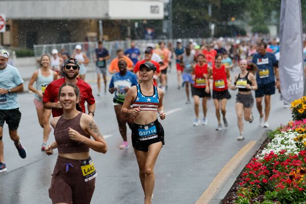 Runners pass along Peachtree Road in Buckhead with light rain at the beginning of the course during the 54th running of The Atlanta Journal-Constitution Peachtree Road Race in Atlanta on Tuesday, July 4, 2023.  The race would later end early because of the weather turning severe.  (Miguel Martinez / Miguel.Martinezjimenez@ajc.com)