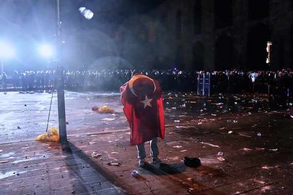 A man with the Turkish flags on his back stands in front of anti riot police officers during clashes in a rally against the arrest of Istanbul's Mayor Ekrem Imamoglu, in Istanbul, Turkey, Friday, March 21, 2025. (AP Photo/Khalil Hamra)