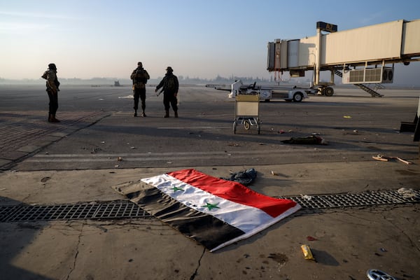 A Syrian official flag lies on the ground as opposition fighters stand on the tarmac of the Aleppo international airpot in Aleppo Monday, Dec. 2, 2024. .(AP Photo/Omar Albam)