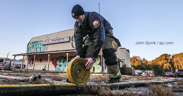 An Atlanta firefighter rolls up a hose line after putting out a fire in a shed behind an abandoned Mexican restaurant.