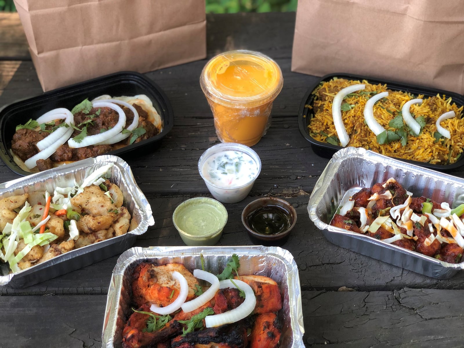 This takeout order from Pinch of Spice in Kennesaw includes (clockwise from upper left): lamb pepper fry, goat biryani, batter-fried cauliflower, tandoori chicken, bamboo fish. Mango lassi and condiments are in the middle. CONTRIBUTED BY WENDELL BROCK