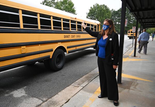 Kara Dutton, principal, waves as school buses arrive at Jackson Elementary School in Lawrenceville on the first day of school for younger students amid the coronavirus outbreak. Gwinnett County Public Schools reports COVID-19 cases by school on its website. (Hyosub Shin / Hyosub.Shin@ajc.com)