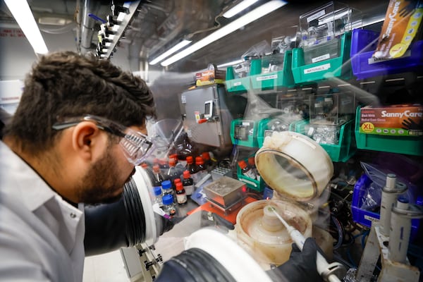 Leonardo Josué Lugo Salas, a visiting graduate student at Georgia Tech, works in an airtight box to add a perovskite liquid to a glass chip in a laboratory inside the Pettit Microelectronics Building at Georgia Tech on Wednesday, March 12, 2025. (Miguel Martinez/AJC)