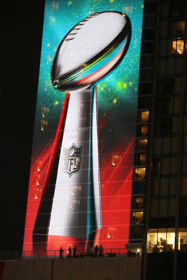 Fans on a Houston hotel balcony are dwarfed by a giant image of the Lombardi Trophy overlooking Super Bowl Live at Discovery Green on Thursday night. (Curtis Compton/ccompton@ajc.com)