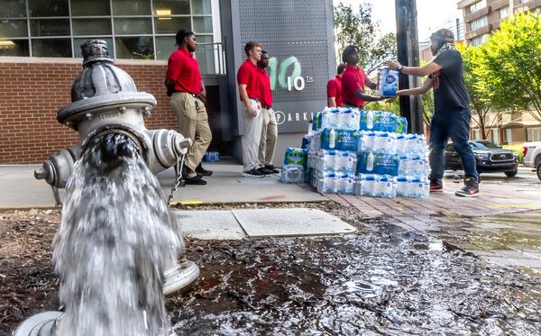 Atlanta Fire Rescue recruits (left) handed out water to Xaku Mitchell (right) on the corner of 10th Street and West Peachtree Street as crews worked Tuesday morning, June 4, 2024 at 11th and West Peachtree Street, one of two significant breaks since Friday afternoon that left thousands in the city with little or no pressure and many other residents forced to boil water. Businesses have also felt the impact and financial woes. (John Spink/AJC)