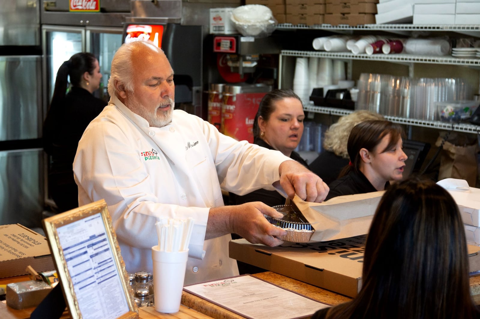 Owner Massimo Fini (C) gets an order ready to go out during the Friday night rush at Fini’s Pizzeria in Lawrenceville. STEVE SCHAEFER / SPECIAL TO THE AJC