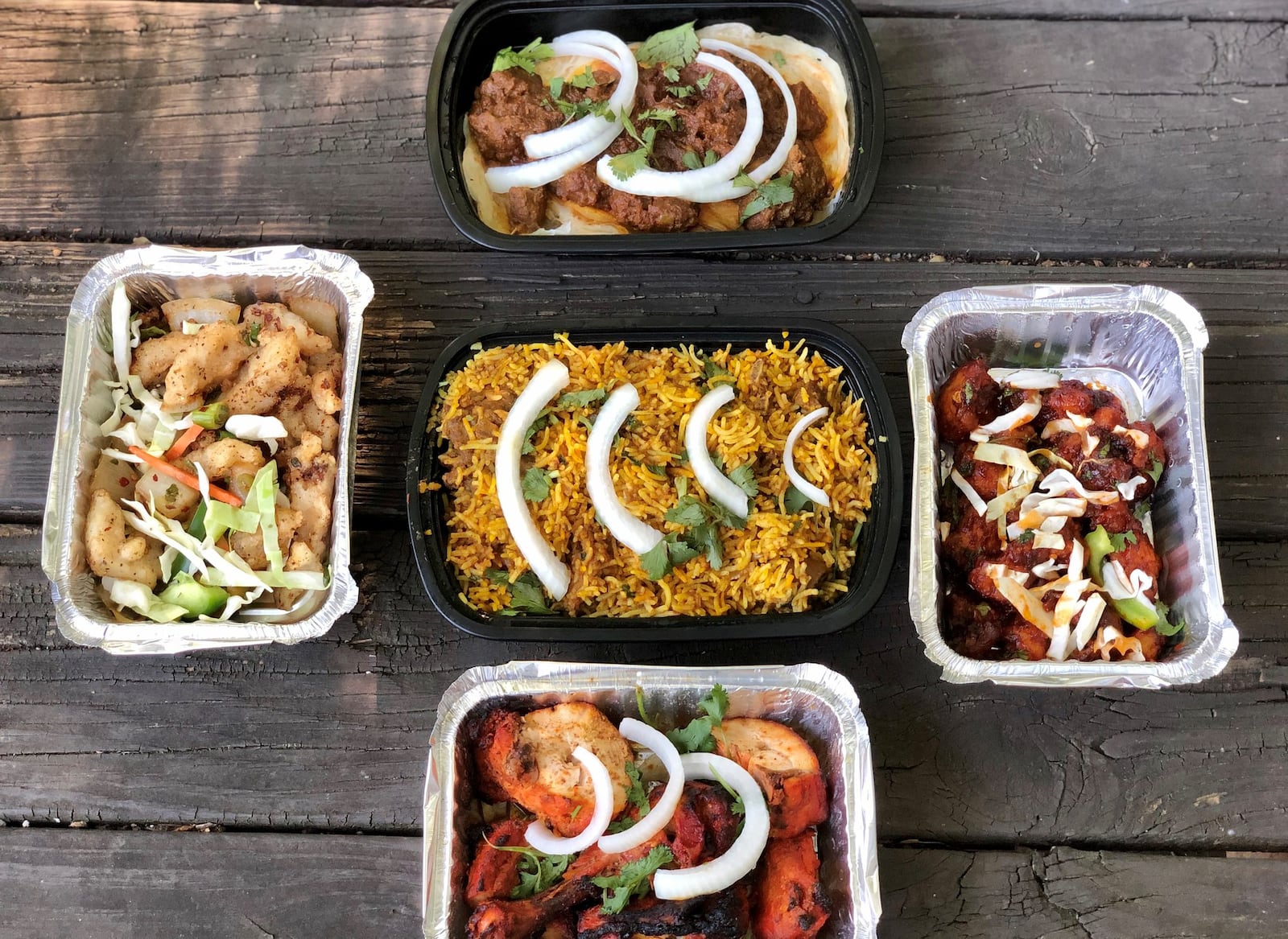 This takeout order from Pinch of Spice in Kennesaw includes (clockwise from top): lamb pepper fry, batter-fried cauliflower, tandoori chicken, bamboo fish and (center) goat biryani. CONTRIBUTED BY WENDELL BROCK