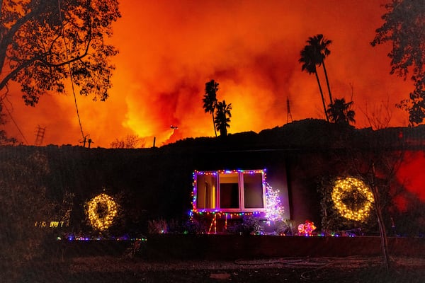 A helicopter drops water on the Palisades Fire behind a home with Christmas lights in Mandeville Canyon, Friday, Jan. 10, 2025, in Los Angeles. (AP Photo/Ethan Swope)