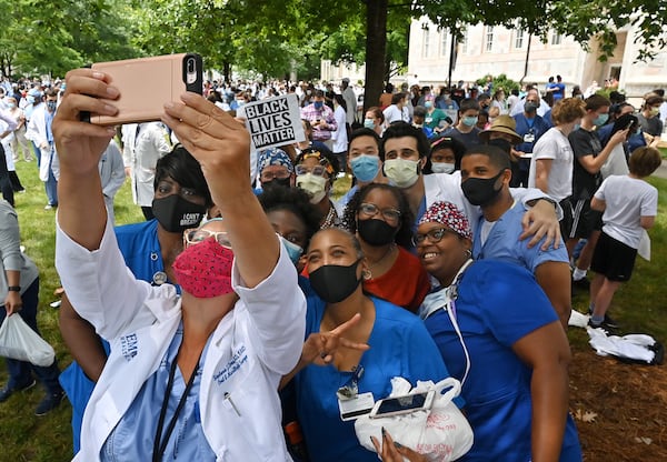 June 5, 2020 Decatur - Stephanie Drew, surgeon, DMD, holds her iPhone to take a selfie group photograph as Emory medical students, doctors, nurses and other health care staff gathered to take a knee for eight minutes and 46 seconds in memory of George Floyd "and countless others," in a demonstration they call White Coats for Black Lives at Emory University Quadrangle on Emory University campus in Decatur on Friday, June 5, 2020. Doctors these days are finding themselves at the intersection of America's race debate: giving advice to protestors on how to protect their eyes from tear gas and speaking their frustration at seeing people of color disproportionately sickened by COVID-19. On Friday at 1pm, a group organized by Emory med students is taking a knee at Emory University for eight minutes and 46 seconds in memory of George Floyd "and countless others," in a demonstration they call White Coats for Black Lives. (Hyosub Shin / Hyosub.Shin@ajc.com)