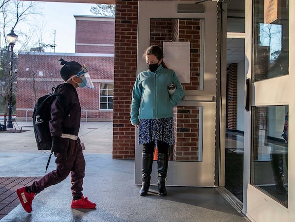 John R. Lewis Elementary School music teacher Elena Prestwood welcomes a student wearing a face shield and a face mask into the school building on the first day of in-person learning in March. (Alyssa Pointer / Alyssa.Pointer@ajc.com)