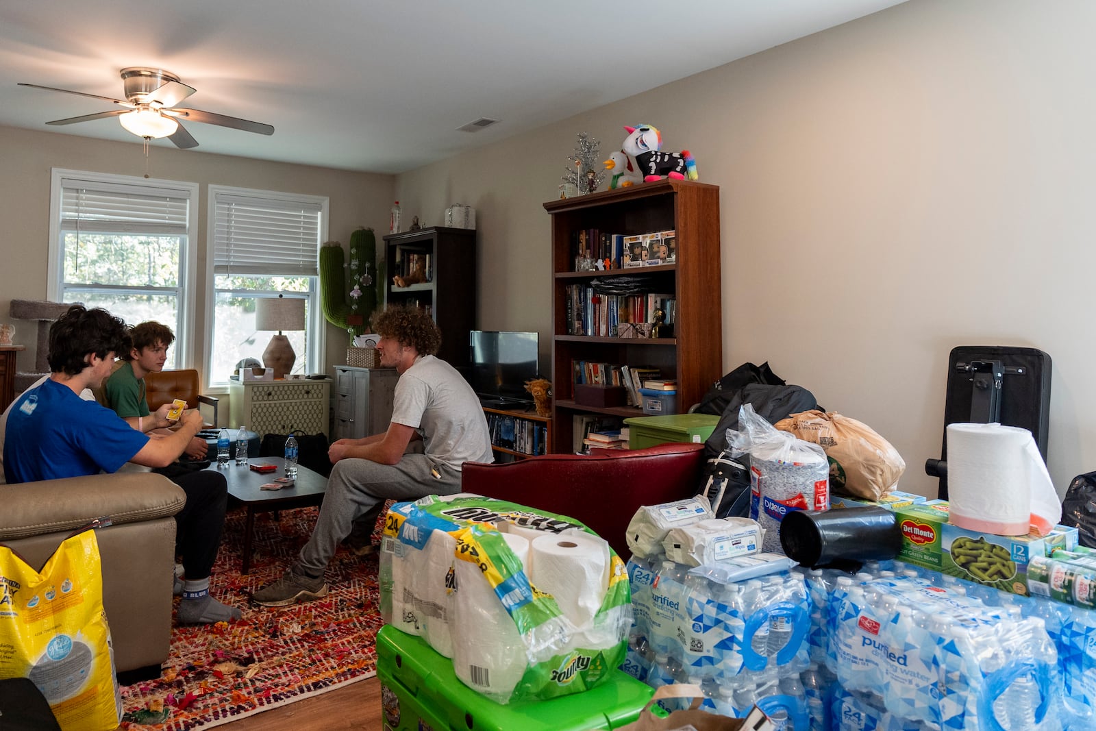 Cases of water, canned food and other supplies are seen in the living room while high school senior Ari Cohen, right, and his friends play a game of Uno, Friday, Oct. 18, 2024, in Asheville, N.C. (AP Photo/Stephanie Scarbrough)