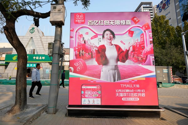 Pedestrians walk near an advertisement promoting a sales festival in Beijing, Thursday, Nov. 7, 2024. (AP Photo/Ng Han Guan)