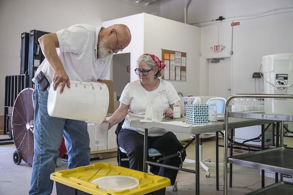 Betsey Dahlberg (right) and Paul Allen, owners of Hope Springs Distillery, work to get every drop of hand sanitizer they created into bottles as they prepare their inventory for their customers at their business in downtown Lilburn. (ALYSSA POINTER / ALYSSA.POINTER@AJC.COM)