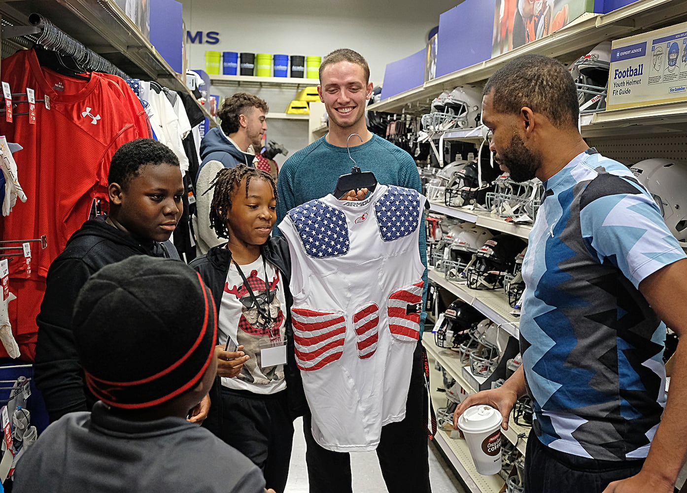 Jalani Evans shows a shirt to his father, Brandon Evans as Carson Best looks on. Carson Beck was on site at an Athens Academy store Sunday December 17, 2023, to give out gift cards to lucky members of area Boys and Girls Clubs. Academy contributed $200 for each child and he kicked in $135 more of his own money to help families out. 

credit: Nell Carroll for the AJC