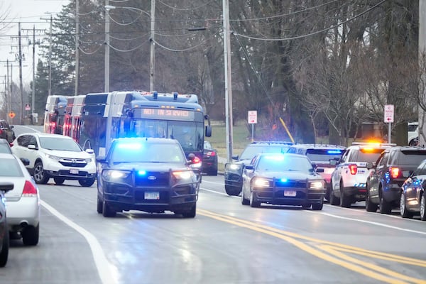 Bus carrying students leave as emergency vehicles are parked outside the Abundant Life Christian School in Madison, Wis., where multiple injuries were reported following a shooting, Monday, Dec. 16, 2024. (AP Photo/Morry Gash)