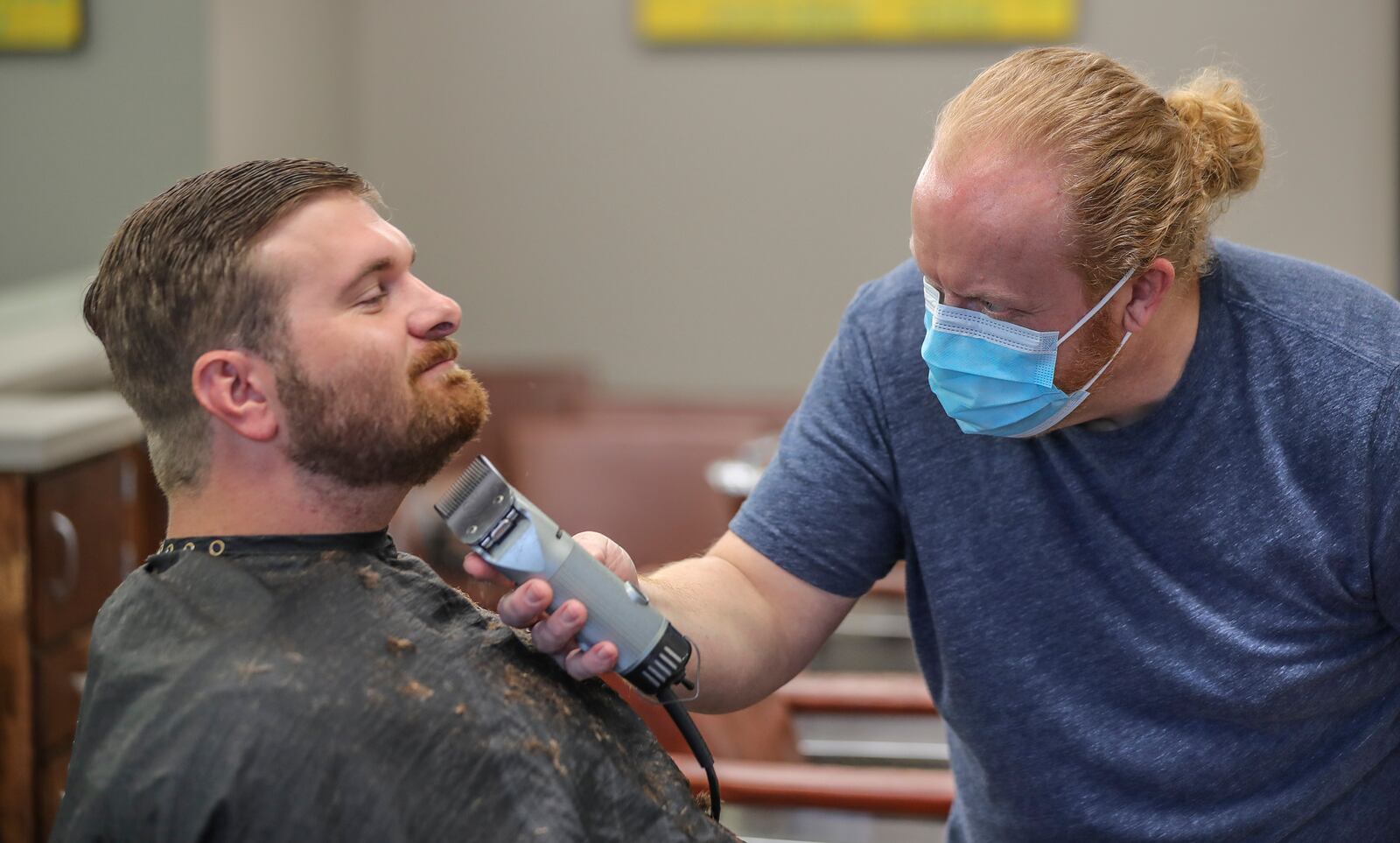 Barber and shop owner Chris Edwards wears a mask and cuts the hair of customer David Boswell at Peachtree Battle Barber Shop at 2333 Peachtree Road in Atlanta on Friday, April 24, 2020. The first phase of Gov. Brian Kemp's plan to reopen Georgia during the coronavirus pandemic included barber shops, hair salons and gyms, though not all chose to open their doors. JOHN SPINK/JSPINK@AJC.COM