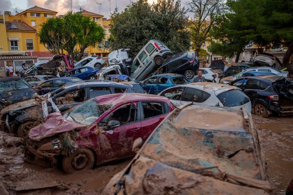 A man stands next to piled-up cars in an area affected by floods in Benetusser, Spain, Saturday, Nov. 2, 2024. (AP Photo/Manu Fernandez)