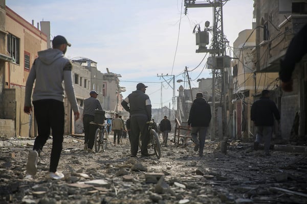 Palestinians walk through the destruction caused by the Israeli air and ground offensive in Rafah, as a ceasefire deal between Israel and Hamas went into effect, Sunday, Jan. 19, 2025. (AP Photo/Mohammad Hajjar)