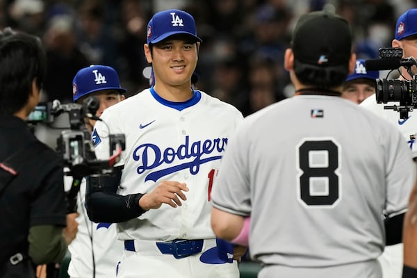 Los Angeles Dodgers' Shohei Ohtani, left, and Yomiuri Giants' Yoshihiro Maru, front, greet each other before the first inning of a spring training baseball game in Tokyo, Japan, Saturday, March 15, 2025. (AP Photo/Hiro Komae)