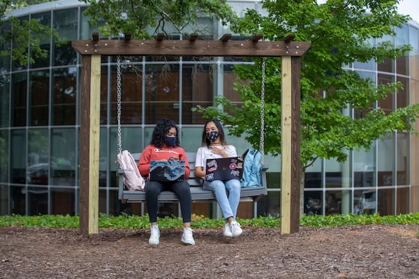 08/17/2020 - Kennesaw, Georgia - Kennesaw State University freshmen Henna Ganesh (left) and Anngie Villlegas (right) wear masks as they socialize on a new bench swing during the first day of classes at Kennesaw State University's main campus in Kennesaw, Monday, August 17, 2020. (ALYSSA POINTER / ALYSSA.POINTER@AJC.COM)