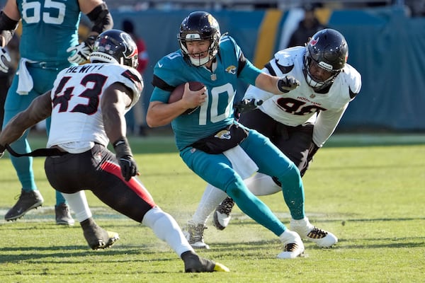 Jacksonville Jaguars quarterback Mac Jones (10) tries to elude Houston Texans linebacker Neville Hewitt (43) and defensive tackle Tim Settle Jr. (98) during the second half of an NFL football game Sunday, Dec. 1, 2024, in Jacksonville, Fla. (AP Photo/John Raoux)