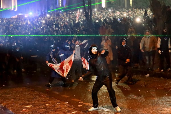 A masked demonstrator throws an object toward police during a rally against the governments' decision to suspend negotiations on joining the European Union for four years, outside the parliament's building in Tbilisi, Georgia, on Sunday, Dec. 1, 2024. (AP Photo/Zurab Tsertsvadze)