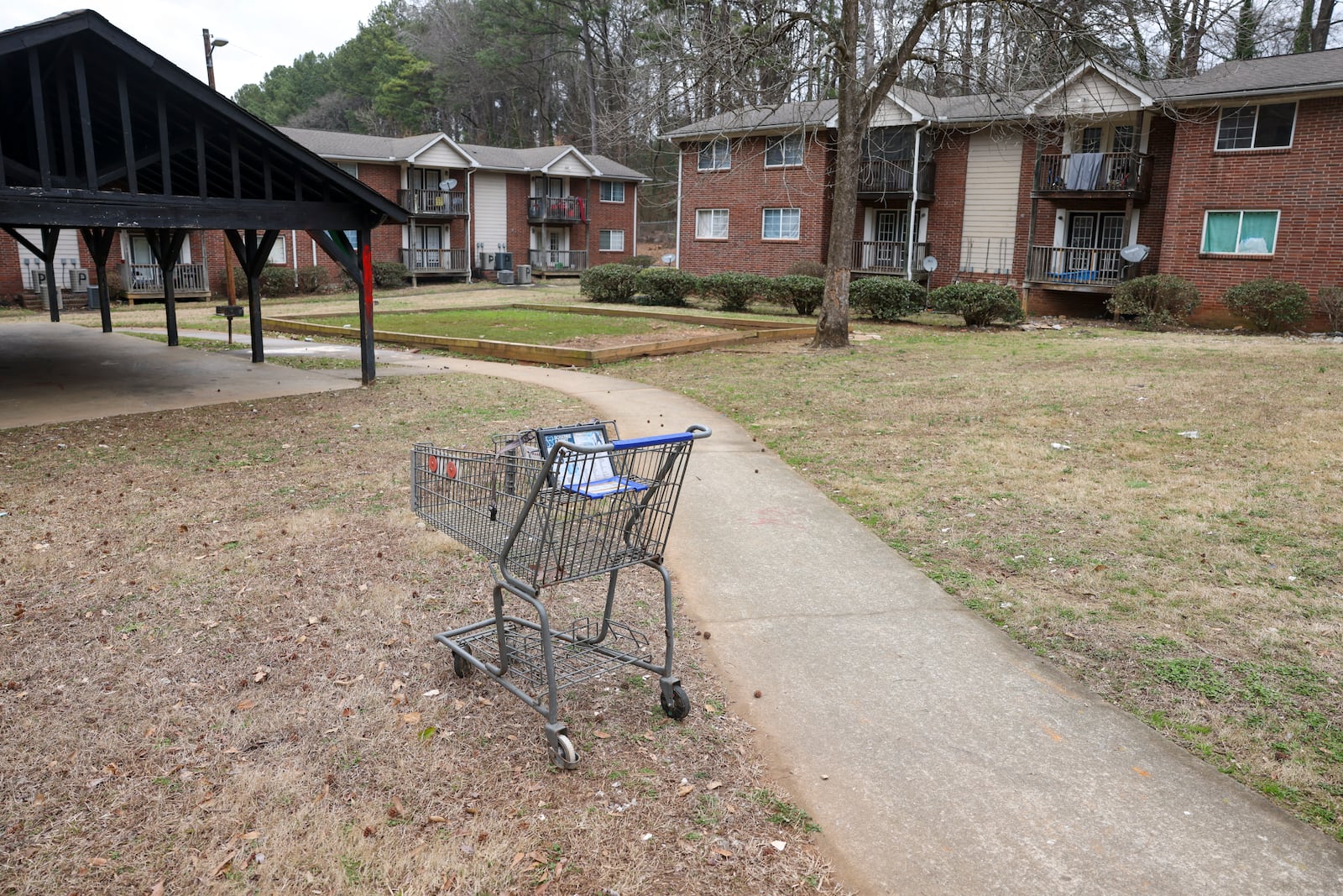 An abandoned shopping cart sits near an empty grass area where the Pavilion Place community playground used to be. Pavilion Place’s owner, Behzad “Ben” Beroukhai, faced 100 criminal counts and $100,000 in fines after code enforcement swept the complex in late 2019. But he didn’t show up for court. (Jason Getz / Jason.Getz@ajc.com)